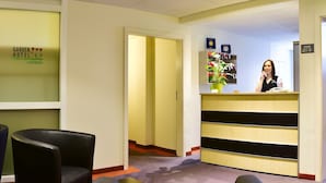 A hotel reception area with a reception desk, a waiting area with chairs, and a carpeted floor. - Garden Hotel (Nuremberg)