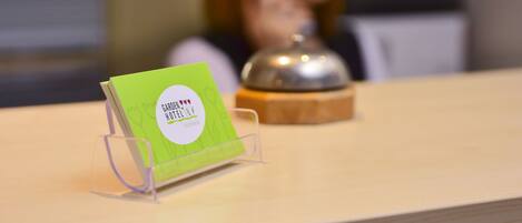 Un mostrador de recepción con un portacartenas verde que muestra el nombre y el logo del hotel.