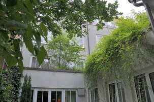 Un edificio con fachada blanca, varias ventanas y un pequeño árbol en la parte delantera.