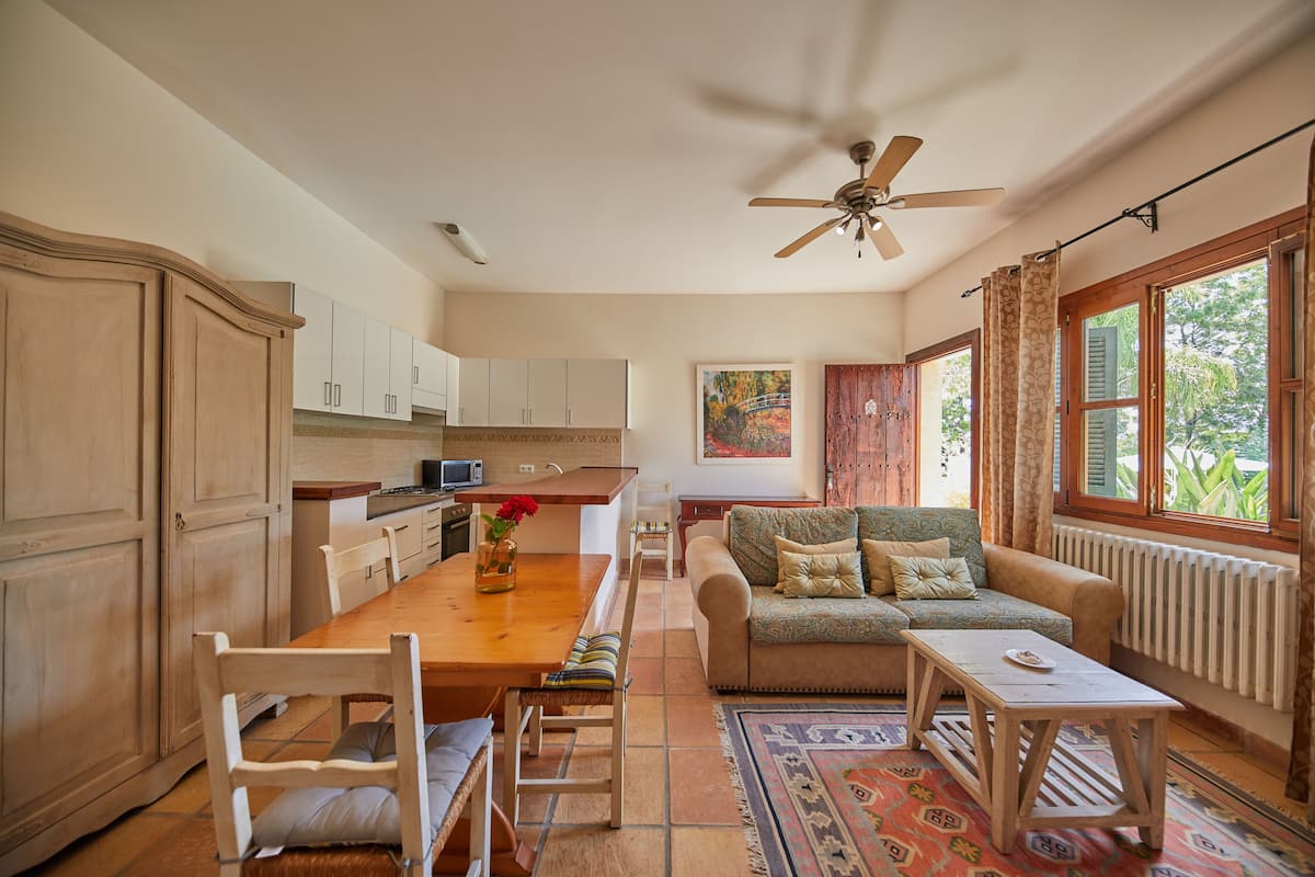 A spacious kitchen with wooden cabinets, a dining table with chairs, a sofa, and a ceiling fan.