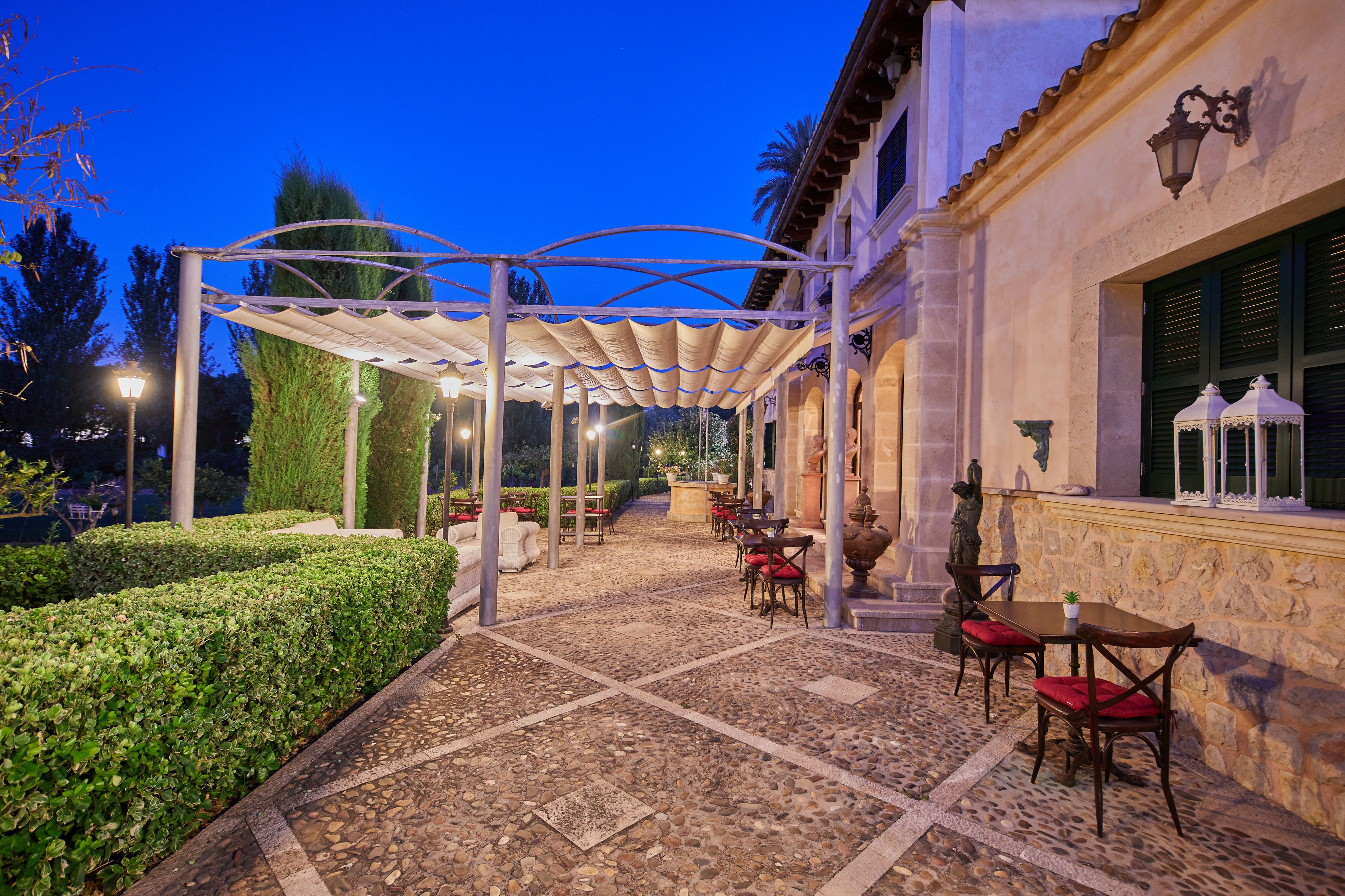 An outdoor patio with tables and chairs, a pergola, and a stone wall.