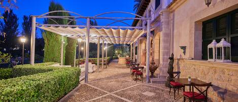An outdoor patio with tables and chairs, a pergola, and a stone wall.