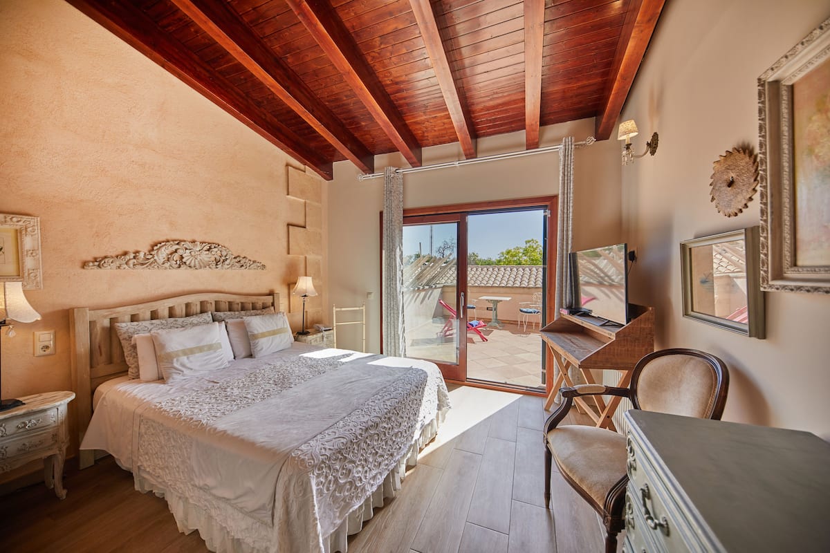 A bedroom with a large bed, wooden ceiling beams, a desk, and a chair.
