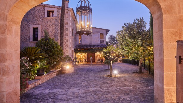 An outdoor courtyard with stone flooring, a building with a balcony, and a hanging lantern. - Sa Vinya des Convent Agroturismo (Inca)