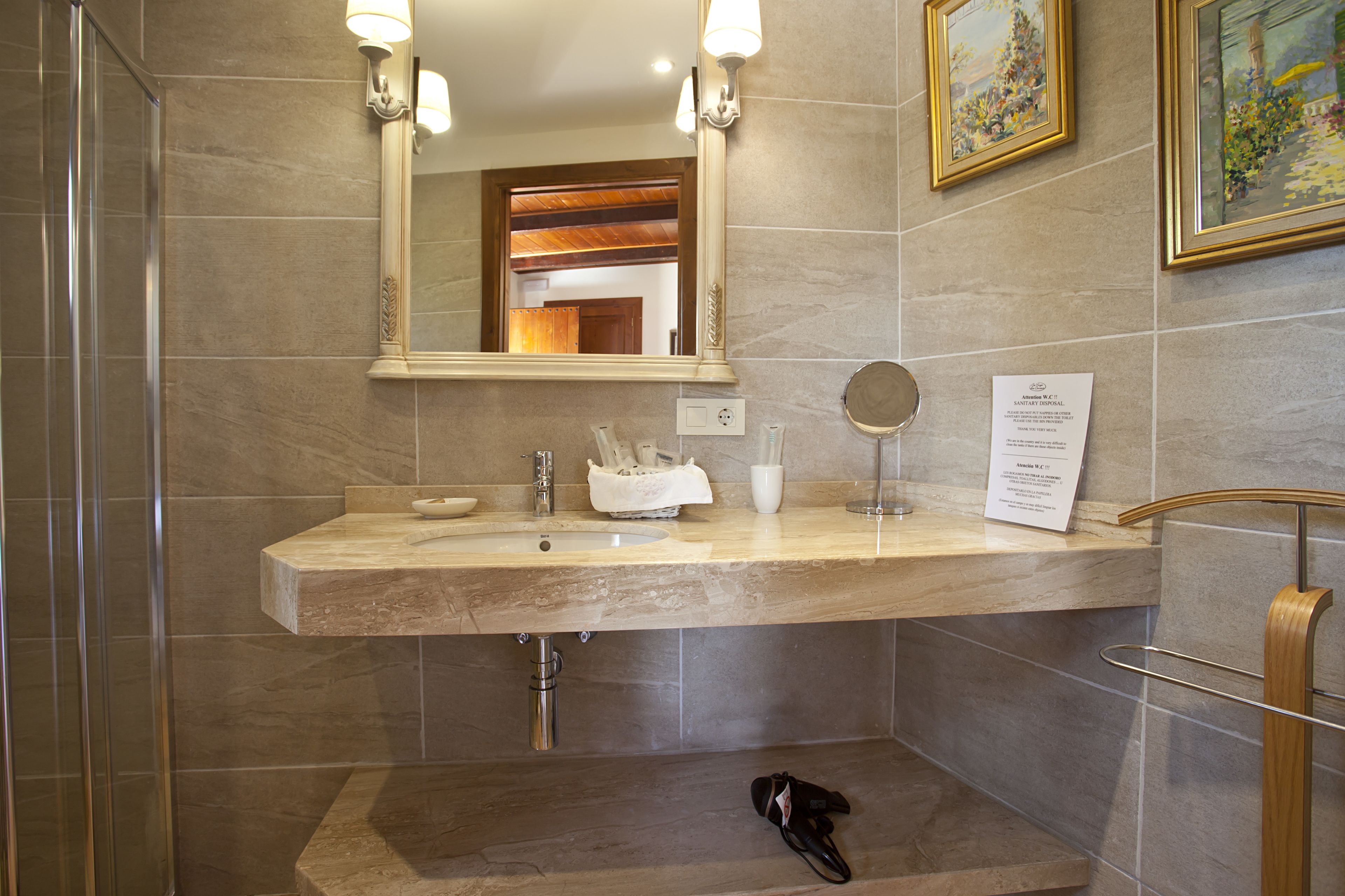 A bathroom with a marble sink, a mirror, a framed picture, and a shoe rack.