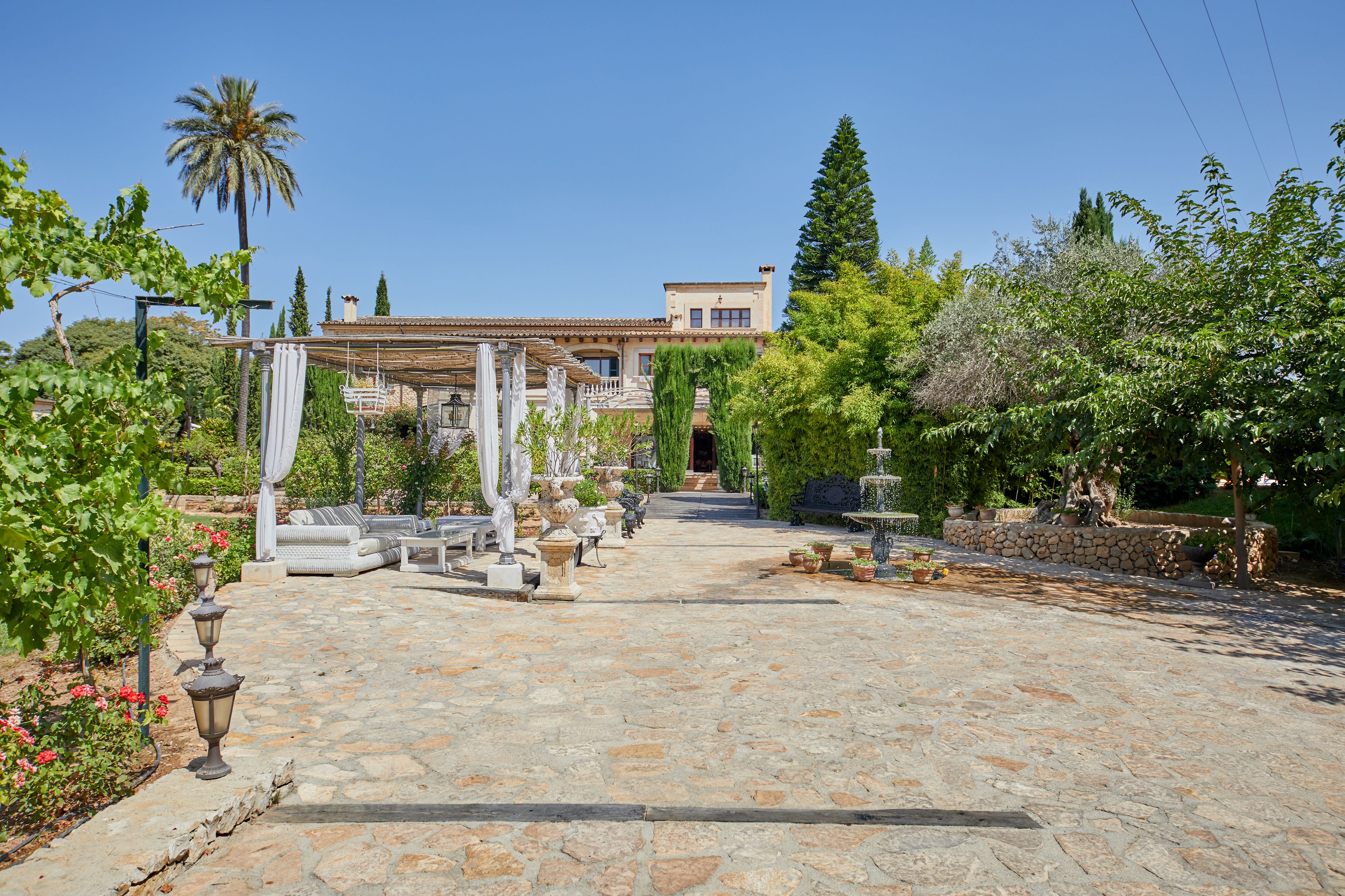A stone-paved courtyard with outdoor seating, a pergola, and a variety of plants and trees.