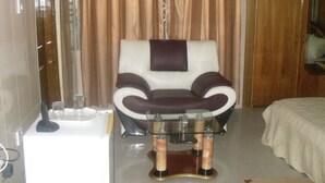 A massage chair in a room with a bathtub, a glass table with bottles, and a bed with a white bedspread. - Senator Hotel (Kumasi)