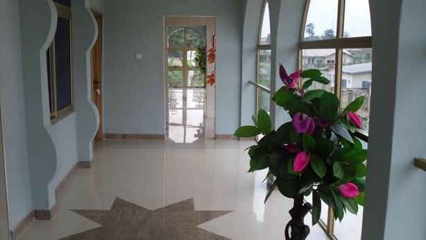 A hallway with a star-patterned floor, large windows, and a potted plant. - Senator Hotel (Kumasi)