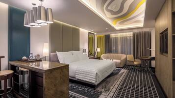 A modern hotel room with a large bed, a desk, a chair, and a small table.