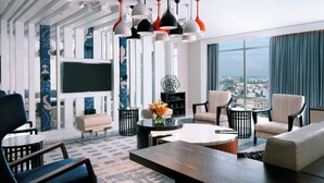 A modern hotel room with a large window, a flat-screen TV, and a variety of seating options including a sofa, chairs, and a coffee table. - Le Meridien Dhaka (Dhaka)