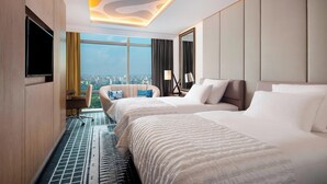A hotel room with two beds, a large window with a city view, a flat-screen TV, and a modern ceiling design. - Le Meridien Dhaka (Dhaka)