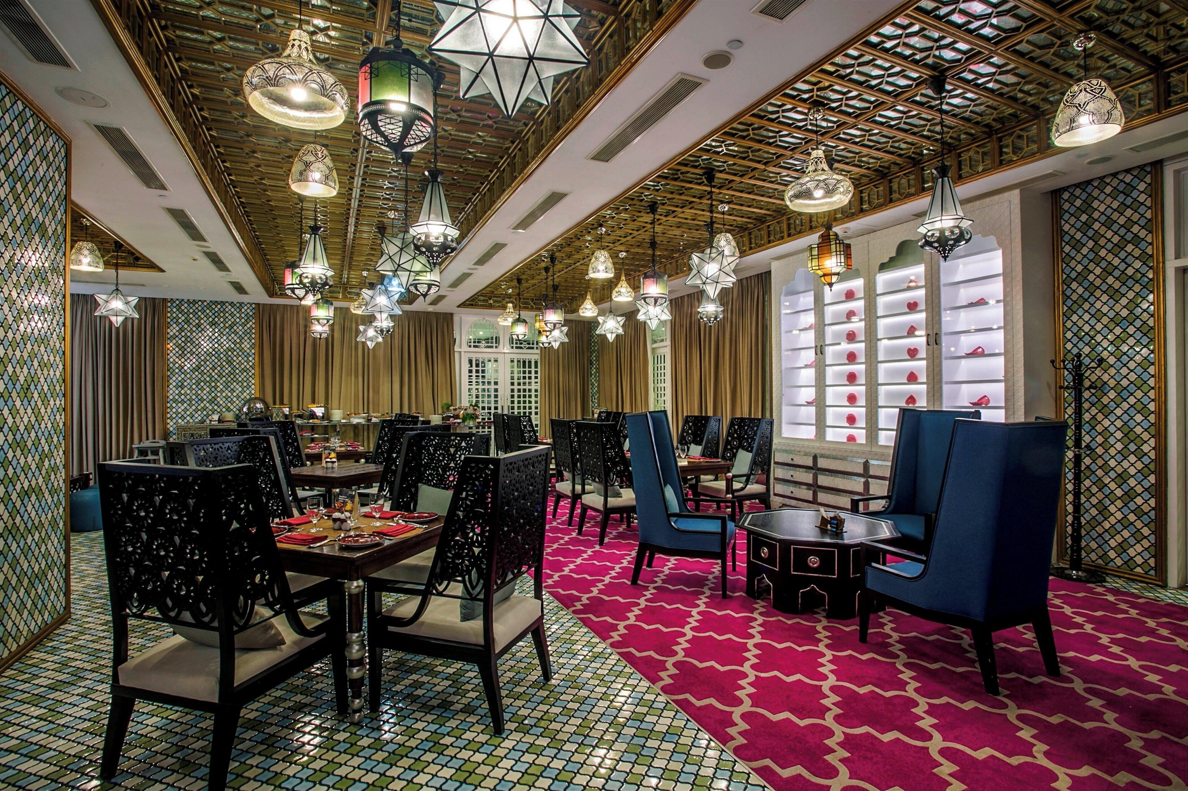 A dining area with multiple tables and chairs, ornate ceiling lights, and patterned walls.