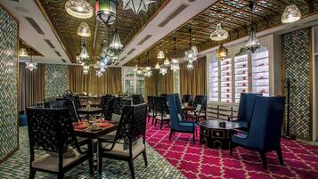 A dining area with multiple tables and chairs, ornate ceiling lights, and patterned walls.