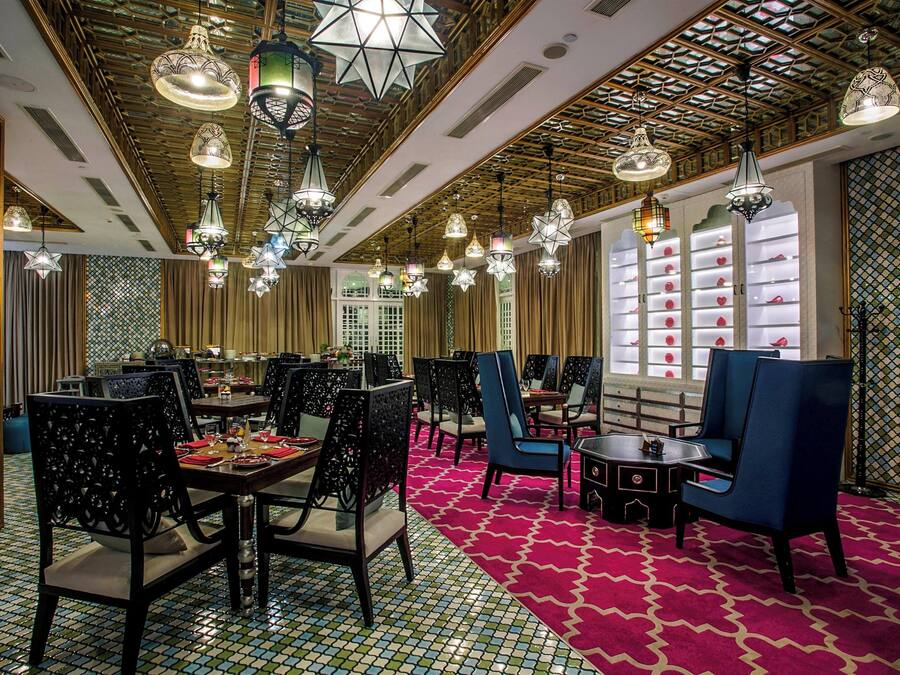 A dining area with multiple tables and chairs, ornate ceiling lights, and patterned walls.