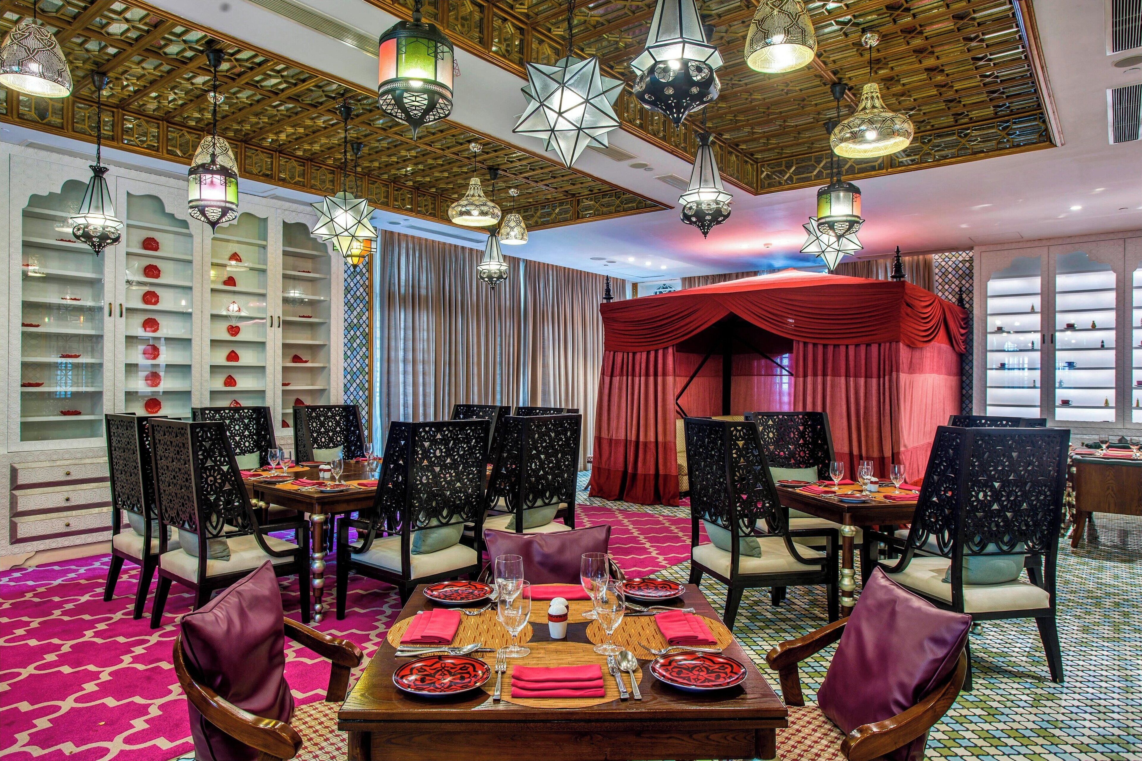 Zona pranzo con tavoli apparecchiati per quattro, circondata da sedie con decorazioni elaborate sullo schienale.