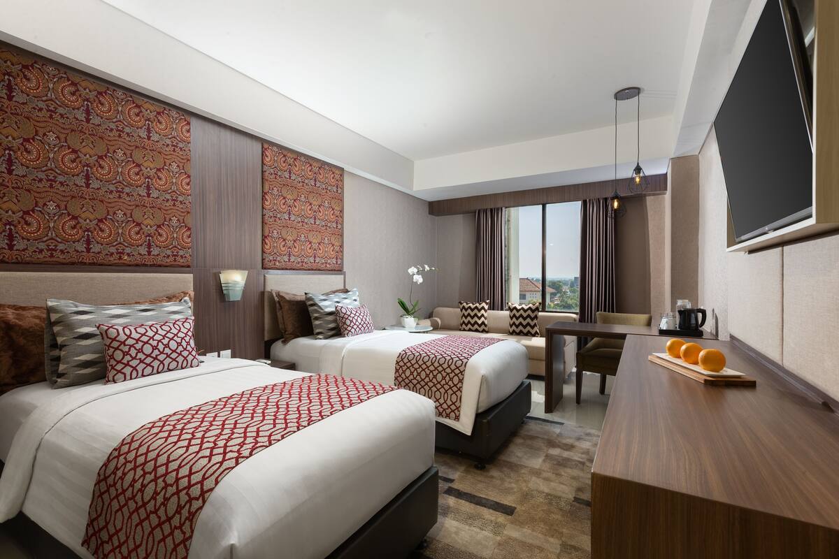 A hotel room with two beds, a dining table, and a TV.