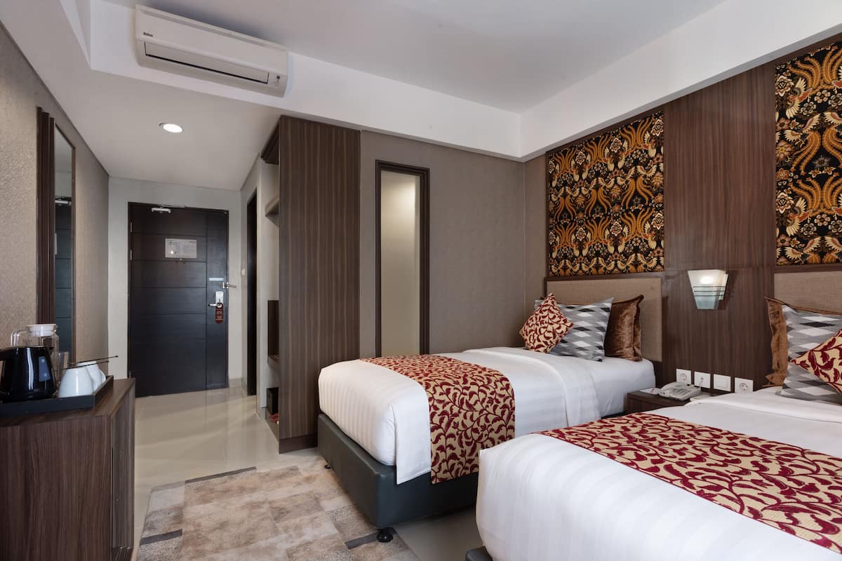 A hotel room with two beds, a desk, and a mirror.
