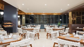 A restaurant with round tables and white wicker chairs, a black oven, and a large window. - The Alana Hotel & Conference Center Malioboro Yogyakarta by ASTON (Yogyakarta)