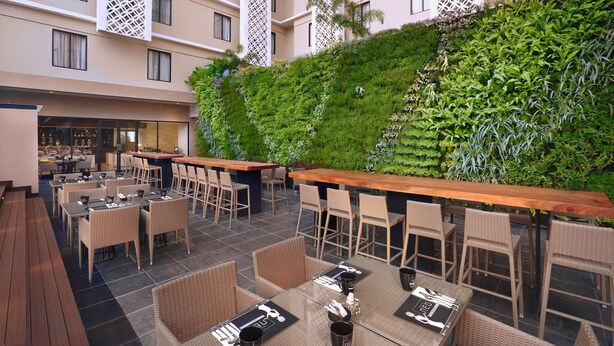 An outdoor seating area with wicker furniture and a wooden bar, surrounded by a lush green wall. - The Alana Hotel & Conference Center Malioboro Yogyakarta by ASTON (Yogyakarta)