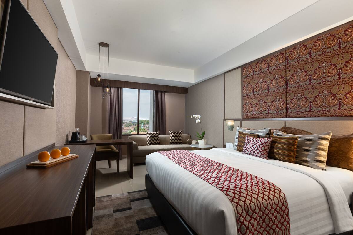 A modern hotel room with a large bed, a desk, a sofa, and a TV.