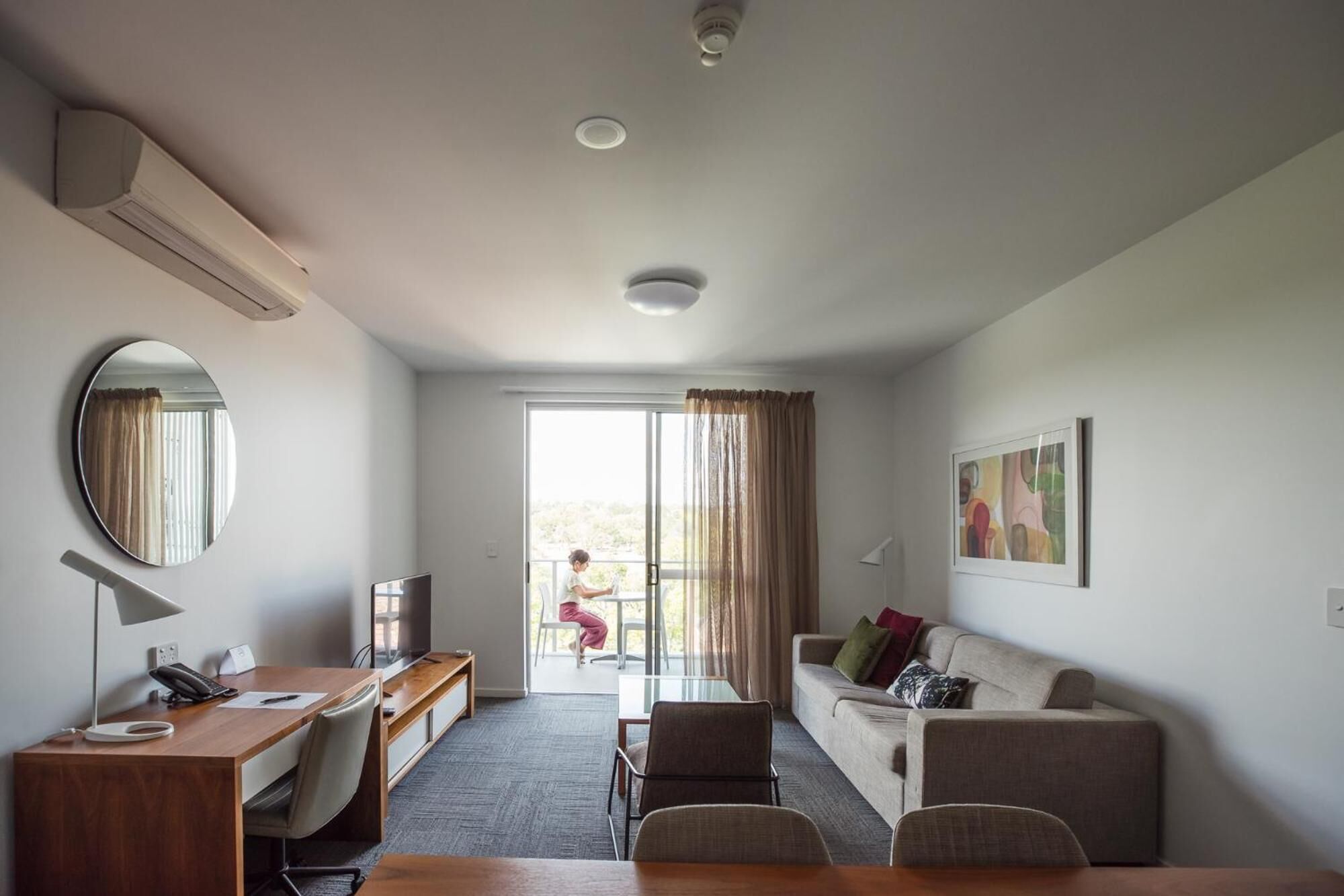 A hotel room with a desk, chair, sofa, and a large window.