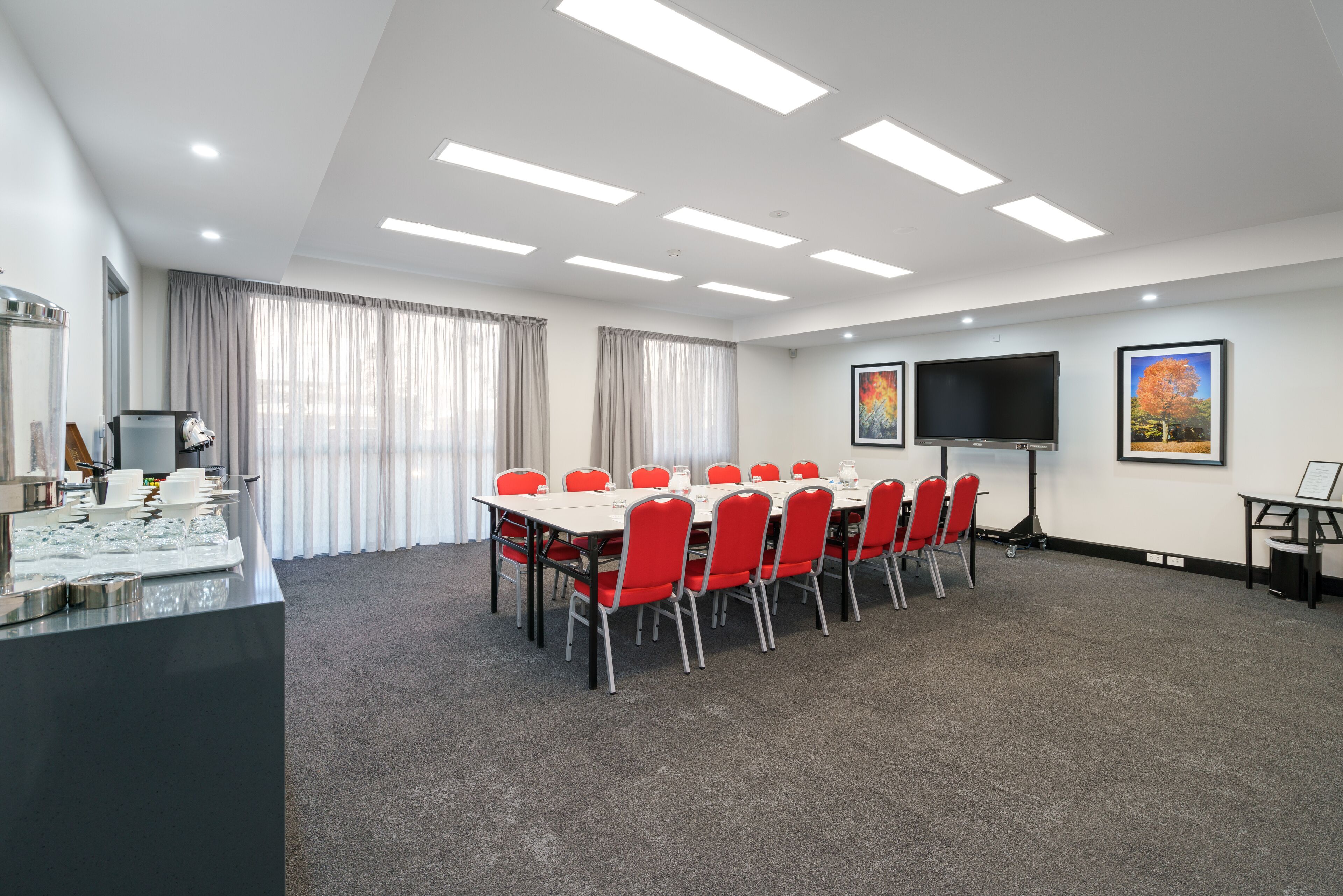 A conference room with a long table, red chairs, a flat-screen TV, and a buffet area.
