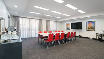 A conference room with a long table, red chairs, a flat-screen TV, and a buffet area.
