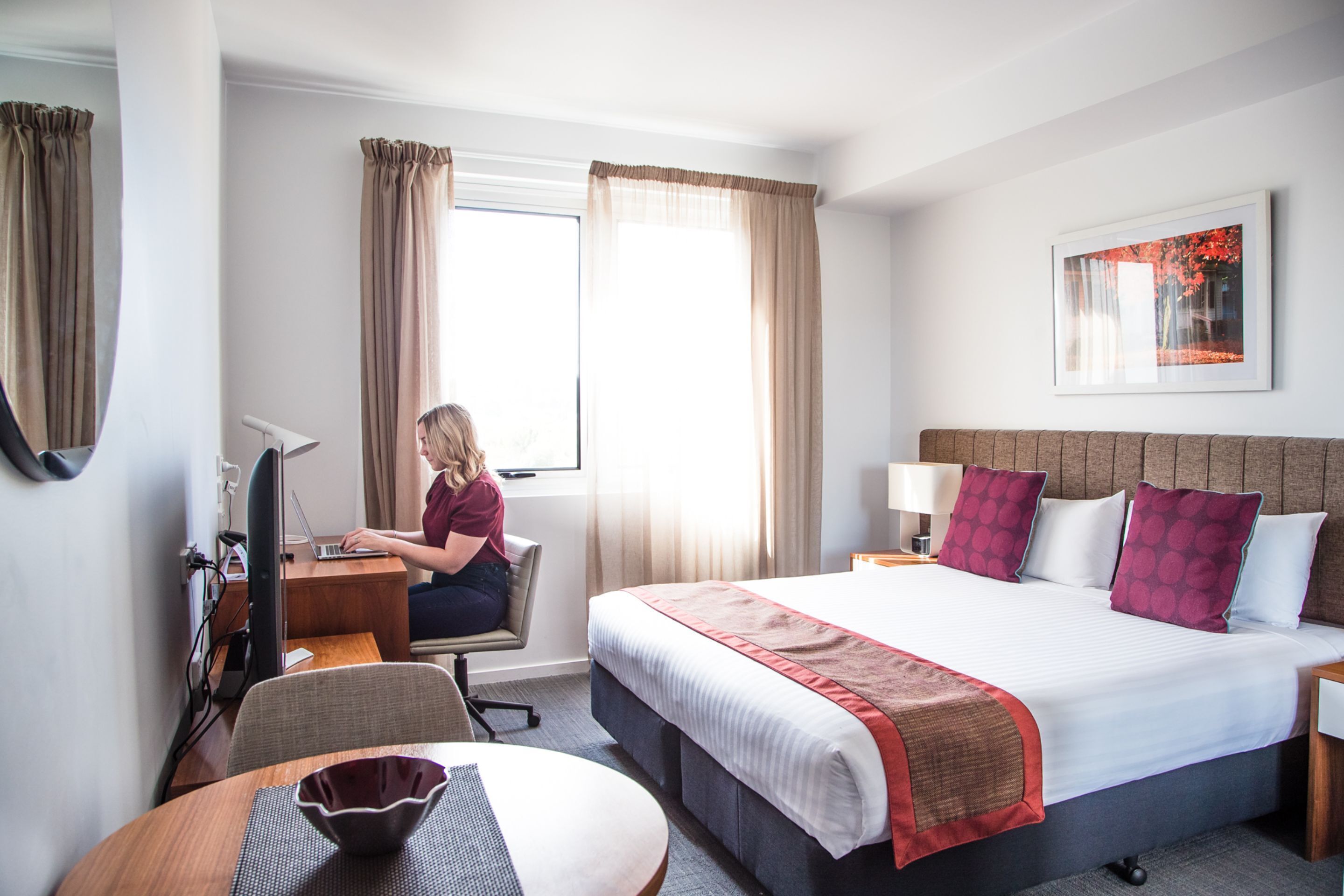 Een hotelkamer met een bed, bureau, stoel en een raam met gordijnen.