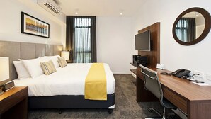 A hotel room with a bed, bedside table, desk, chair, TV, and a mirror. - Quest Rockingham (Rockingham)