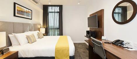 A hotel room with a bed, bedside table, desk, chair, TV, and a mirror.