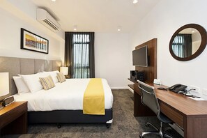 A hotel room with a bed, bedside table, desk, chair, TV, and a mirror.