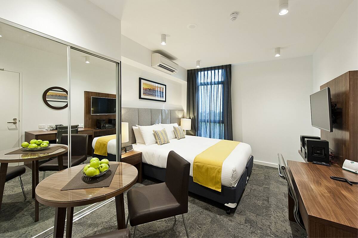 A hotel room with a bed, bedside table, chair, desk, and a dining area with a table and chairs.