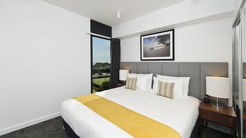 A hotel room with a large bed, a bedside table, a lamp, a framed picture on the wall, and a window with a view.