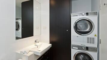 Een moderne badkamer met een grote spiegel, een wastafel en gestapelde wasmachines.