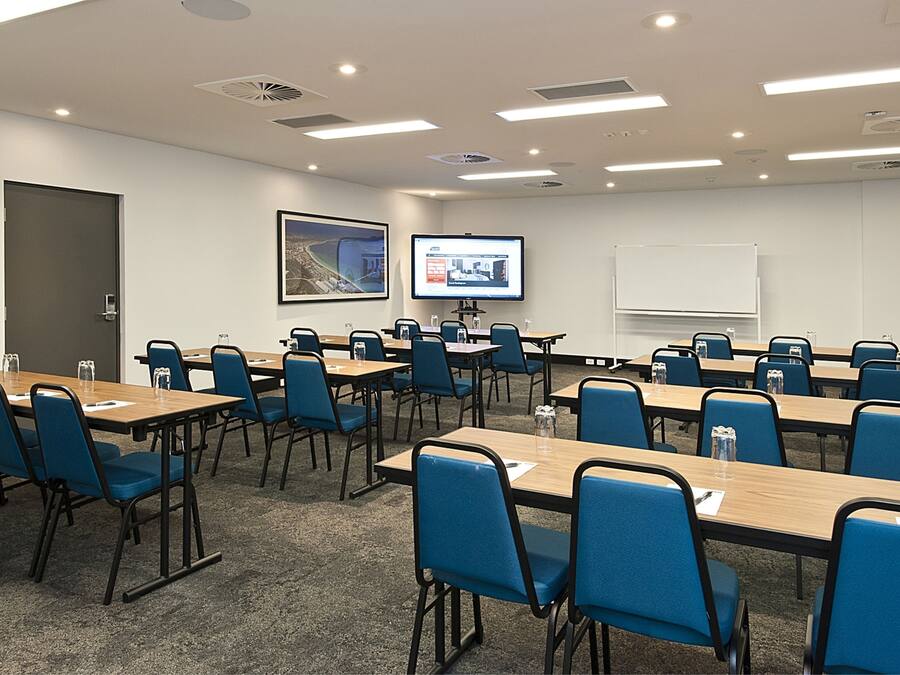 Una sala de conferencias con varias mesas y sillas, una pantalla de proyector y una pizarra.