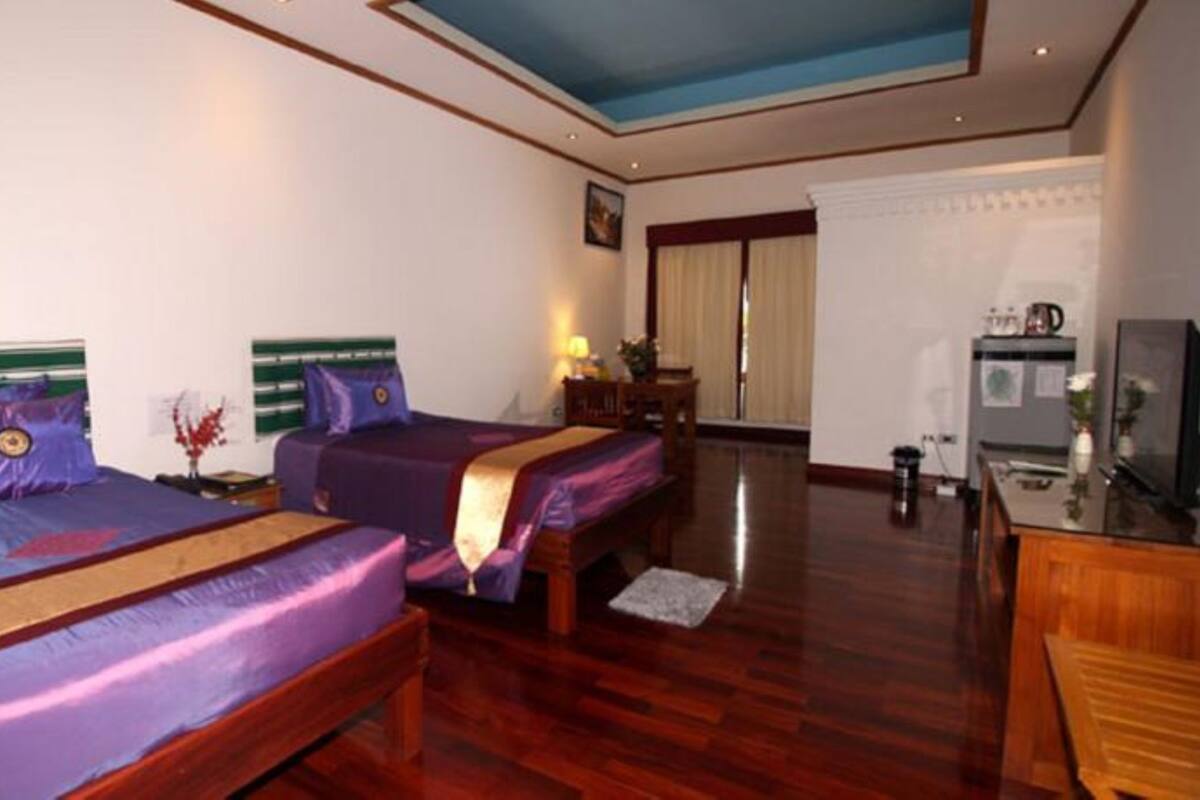 A hotel room with two beds, wooden flooring, a desk, a television, and a window with curtains.