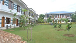 A courtyard with a lawn, trees, and a building with multiple windows and doors. - Myanmar Life Hotel (Yangon)