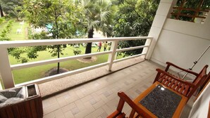 A balcony with a view of a garden, a wooden chair, and a small table. - Myanmar Life Hotel (Yangon)