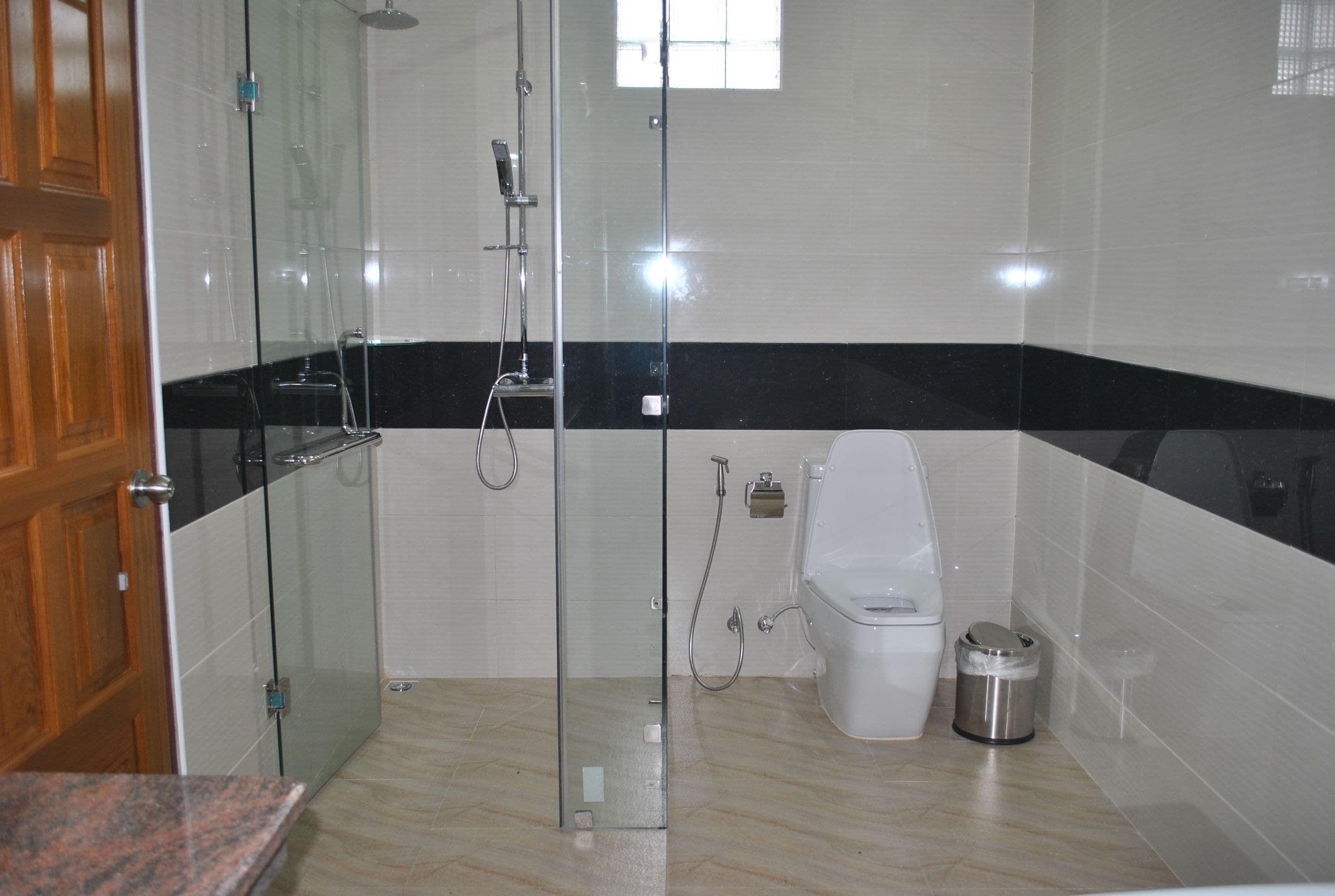 A bathroom with a glass-enclosed shower, a toilet, and a trash bin.