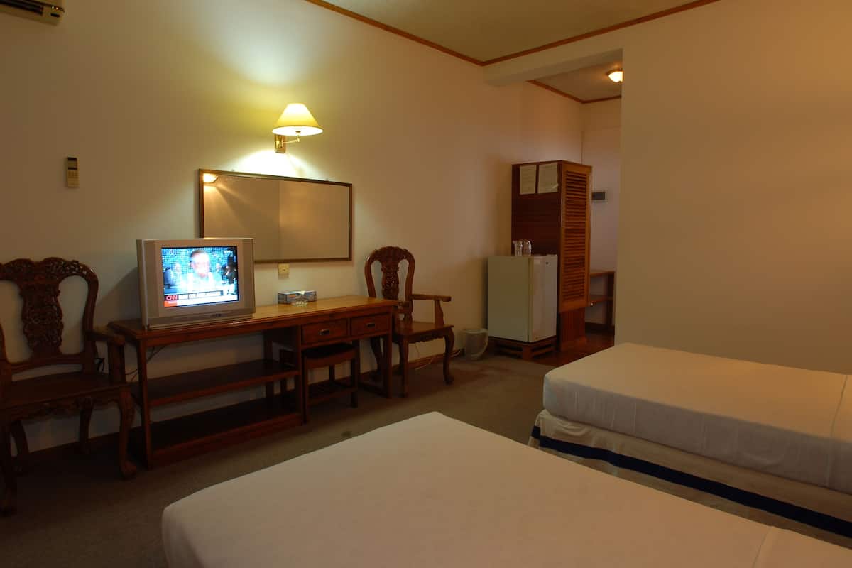 A hotel room with two beds, a desk with a television, a mirror, and a refrigerator.