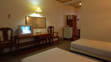 A hotel room with two beds, a desk with a television, a mirror, and a refrigerator.