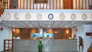 A hotel reception area with a counter, multiple clocks, and a wooden staircase. - Myanmar Life Hotel (Yangon)