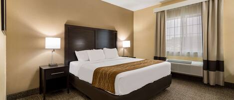 A hotel room with a large bed, two bedside tables with lamps, a window with curtains, and a wall-mounted air conditioning unit.