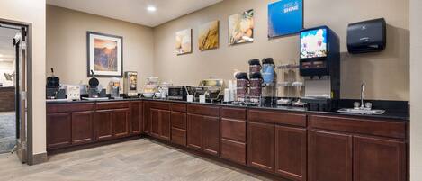 A hotel reception area with a long counter, coffee machines, and a television screen displaying a program.
