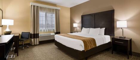A hotel room with a large bed, a desk, a chair, a nightstand, and a window with curtains.