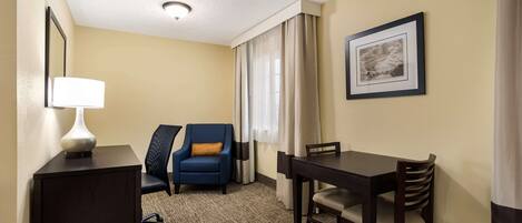 A hotel room with a desk, a chair, a sofa, a dining table, and a picture on the wall.