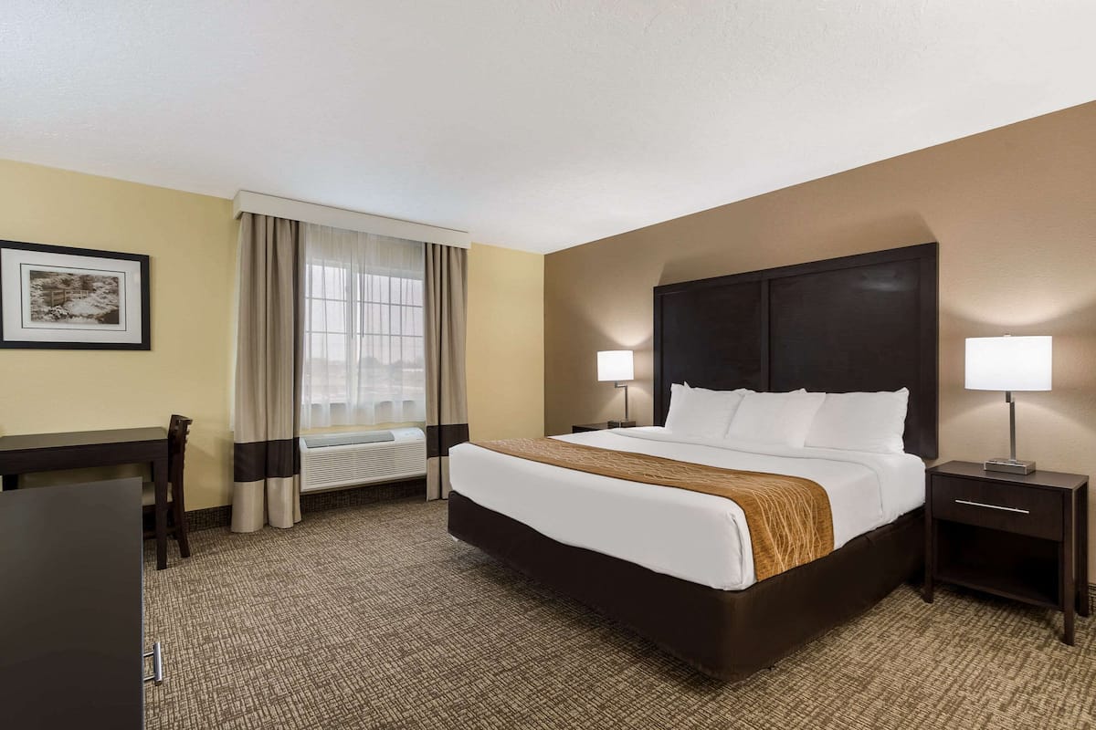 A hotel room with a large bed, two bedside tables with lamps, a desk, and a chair.