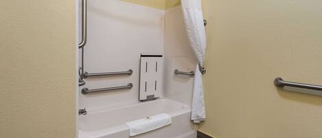 A bathroom with a white bathtub, grab bars, a towel rack, and a shower curtain.