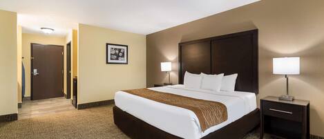 A hotel room with a large bed, two bedside tables, a headboard, and a carpeted floor.