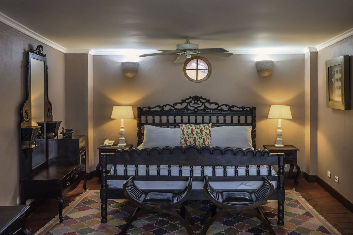 Un dormitorio con una cama grande, dos mesitas de noche, un ventilador de techo y una alfombra estampada.